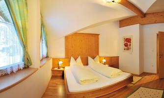 A cozy bedroom with two single beds and warm wooden details. Natural light pours in through the windows, creating an inviting atmosphere.