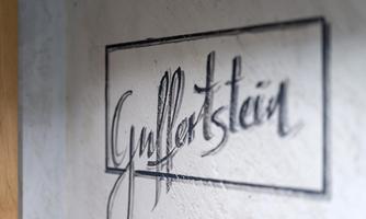 A piece of art named "Gyllertstein" in an elegant font. The inscription is located on a light wall.