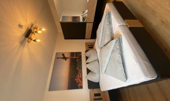 A modern bedroom with a large bed and cozy pillows. A picture hangs on the wall and there is a mirror that expands the space.