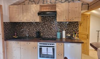 A modern kitchen made of wood with a stylish tile backsplash. The amenities include a stove, refrigerator, and numerous kitchen utensils.
