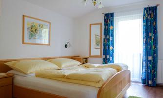 A cozy bedroom with a large double bed and a single bed. Light colors and a balcony create a pleasant atmosphere.