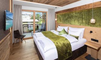 A modern bedroom with a large bed and stylish wood design. The room provides access to a balcony with a view of the landscape.