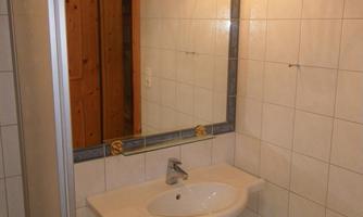 A small bathroom with a sink, mirror, and shower. The walls are tiled, and there is pleasant lighting.