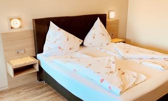 A cozy bedroom with a large double bed and two bedside tables. The walls are painted in neutral colors, and a decorative picture hangs above the bed.