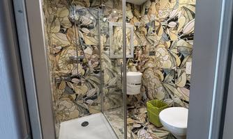 A modern bathroom with a glass shower and a stylish, floral wall design. The room includes a toilet and a sink.