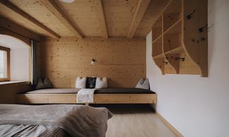 A cozy bedroom with wooden paneling and a large window. The room is simply furnished and has an inviting atmosphere.