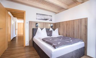 A cozy bedroom with a large bed and wooden details. The walls are light, and there is a pleasant, inviting atmosphere.