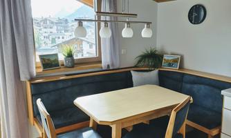 A cozy dining area with an oval table and a bench. A beautiful view of the surroundings can be seen through the window.