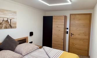 A modern bedroom with a double bed and cozy bedding. The room features a bright decor and a wooden dresser.