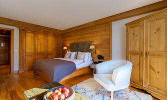 A cozy bedroom with wooden walls and a large bed. A comfortable armchair and a table with apples complete the room.