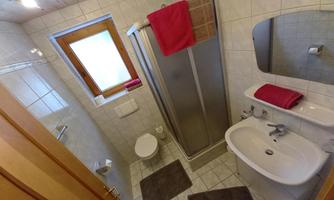 A modern bathroom with tiles and a shower area. There is a sink, a toilet, and towels in bold colors.