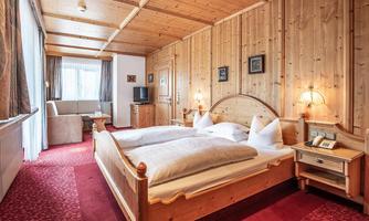 A cozy bedroom with wood paneling and a double bed. The furnishings are rustic with a red carpet and a comfortable armchair.