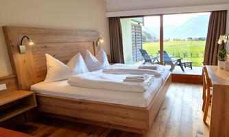 A modern room with wooden details and two beds. There is a balcony with a view of the green countryside and mountains.
