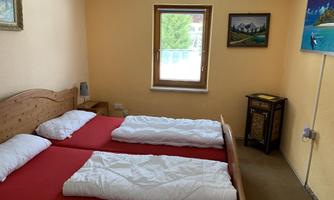 A simple room with two single beds and red bedcovers. The room has a window that lets in light and is decorated with pictures on the walls.