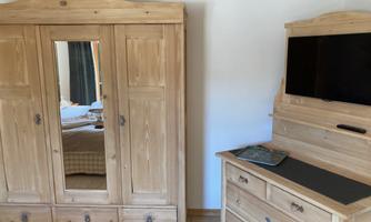 A cozy room with a wooden wardrobe and a dresser. The wardrobe has a mirror, and the dresser has a television on it.