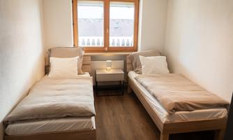 A simple room with two single beds and a nightstand. The window lets in plenty of daylight.