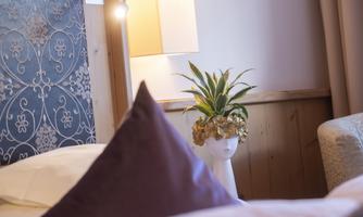 A cozy bedroom with an elegant pillow and a decorative lamp. A plant in a special vase shaped like a head adds an artistic touch.