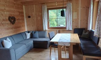 A cozy living space with wooden ceilings and light walls. A gray couch and a table invite you to relax.