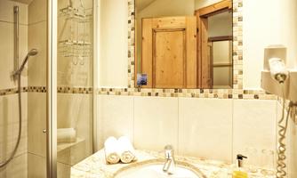 A modern bathroom with a shower and a sink. On the shelf are white towels, and in the background, a wooden door frame is visible.