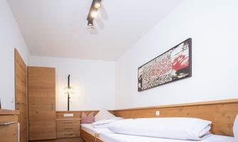 A modern bedroom with two single beds and a minimalist design. A decorative artwork hangs on the wall, and the room features clear, bright colors.