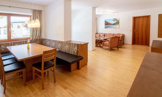 A modern dining room with a large wooden table and chairs. The room is bright and welcoming, with wooden floors and large windows.