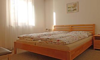 A cozy bedroom with two beds and light wood. The windows let in plenty of natural light.