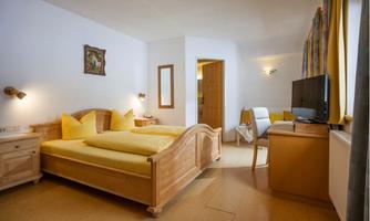 A modern bedroom with two single beds and yellow bedcovers. The room is bright and cozy furnished with a table, chair, and a TV.
