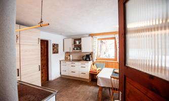 A modern kitchen with bright wooden cabinets and a cozy dining area. Light pours in through the window, creating an inviting atmosphere.