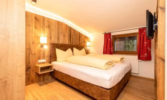 A cozy bedroom with a double bed and wooden walls.  
Large windows and red curtains create an inviting atmosphere.