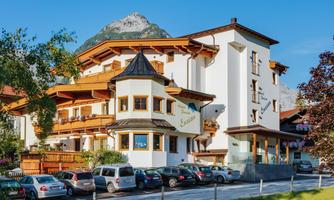 A charming hotel with traditional architecture and a beautiful mountain in the background. In front of the building, many cars are parked in a parking lot.