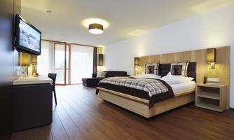 A modern hotel room with a large bed, stylish furniture, and warm wooden flooring. It features a television and a view of a balcony.