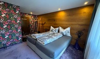 A stylish bedroom with a double bed and elegant bedding. The walls are decorated with a colorful floral pattern and wood look.