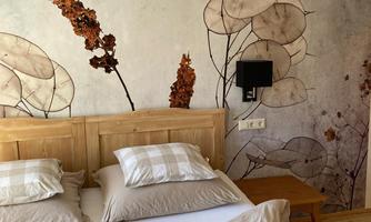 A cozy bedroom with a wooden bed frame and light, natural-colored bedding. The wall is decorated with a calming plant motif wallpaper.