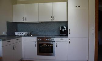 A modern kitchen with white cabinets and a gray workspace. It is well-equipped with a stove, a sink, and appliances.