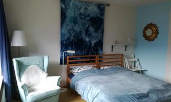 A cozy bedroom with a large bed and a light blue wall. An armchair and a decorative wall design with a maritime motif complete the room.