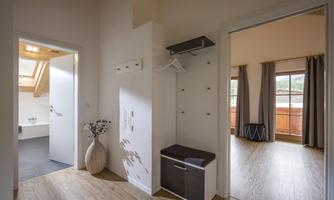A bright hallway with a white wall closet and a coat rack. In the background, windows with curtains and a balcony are visible.