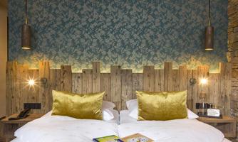 A cozy bedroom with two beds and golden pillows. The wood details and the stylish wall design create a relaxed atmosphere.