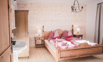 A cozy bedroom with a double bed and checkered bedding. The walls are made of light wood, and there is a window as well as an elegant ceiling lamp.