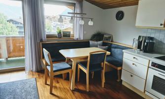 A cozy kitchen corner with a wooden table and chairs. Large windows provide plenty of daylight and a view outside.
