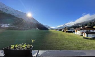 A beautiful landscape with a green meadow in the foreground and mountains in the background. The sun is shining brightly in the sky.