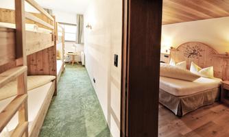 A cozy room with a bunk bed on the left and a double bed on the right. The room is bright and welcoming with green carpet flooring.