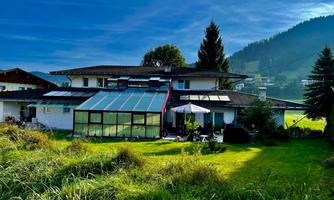 A large house with a conservatory and a green lawn in the foreground. In the background, gentle hills and trees can be seen.