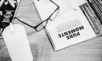 A pair of glasses lies on an open magazine titled "PURE WOMEN". Next to it is a candle on a coaster.