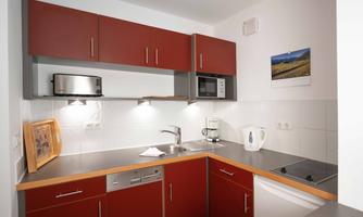 A modern kitchen with red cabinets and a gray countertop. It is equipped with a microwave, a kettle, and a coffee machine.