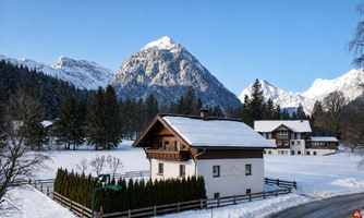 A picturesque winter landscape with snow-covered mountains and a charming house. The trees are covered in snow, and the sky is clear and blue.