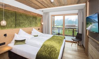 A modern bedroom with wooden decor and comfortable beds. Large windows offer a view of the surrounding landscape.