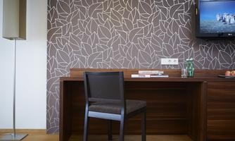 A modern room with a desk and a chair. A decorative leaf pattern is on the wall, and a television is visible.