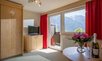 A cozy room with a large window and a view of the mountains. A table with flowers and champagne complements the bright, inviting atmosphere.