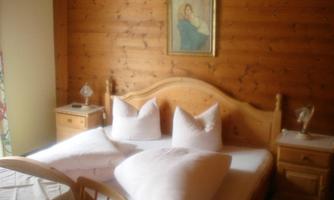 A cozy bedroom with wooden walls and a double bed. On the nightstand, there is a lamp, and a picture hangs on the wall.