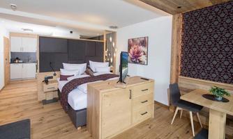 A modern room with wooden flooring and stylish furniture. The room features a double bed, a small kitchenette, and a dining area.